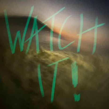 Artwork for the song 'Watch It!' by Nuri, featuring a blurred, abstract background with green handwritten text 'WATCH IT!' prominently displayed in the center. The background colors blend together in a soft, swirling pattern, creating a sense of movement and urgency.